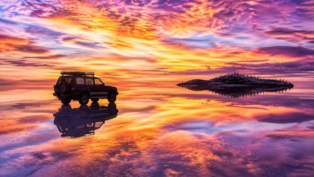 Salar de Uyuni Bolivia salt flat mirror reflection at sunrise with lone vehicle silhouette